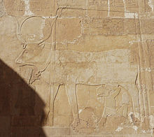 Relief of a cow with a disk between her horns. A human wearing a crown drinks from her udders.