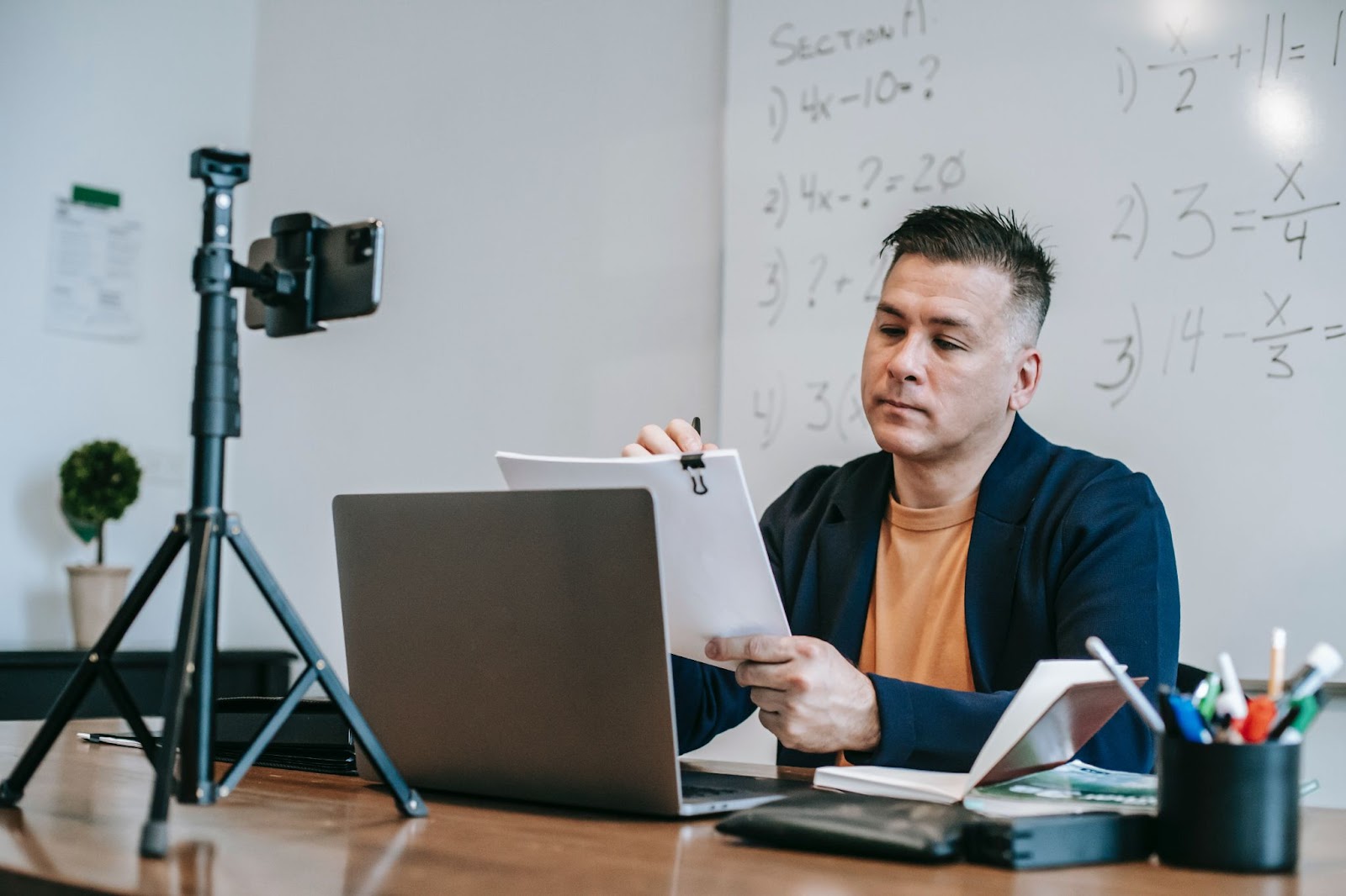 Man at Desk Reading Papers with WhiteBoard Behind Him