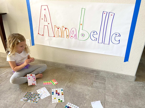 Anabelle written on large paper taped to the wall with girl decorating it 