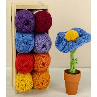 knitted flower in terra cotta pot next to a crate with colorful skeins of yarn inside