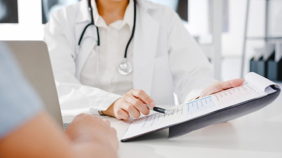 Médico sentado em frente a computador e a paciente em consulta por assistência médica coletiva