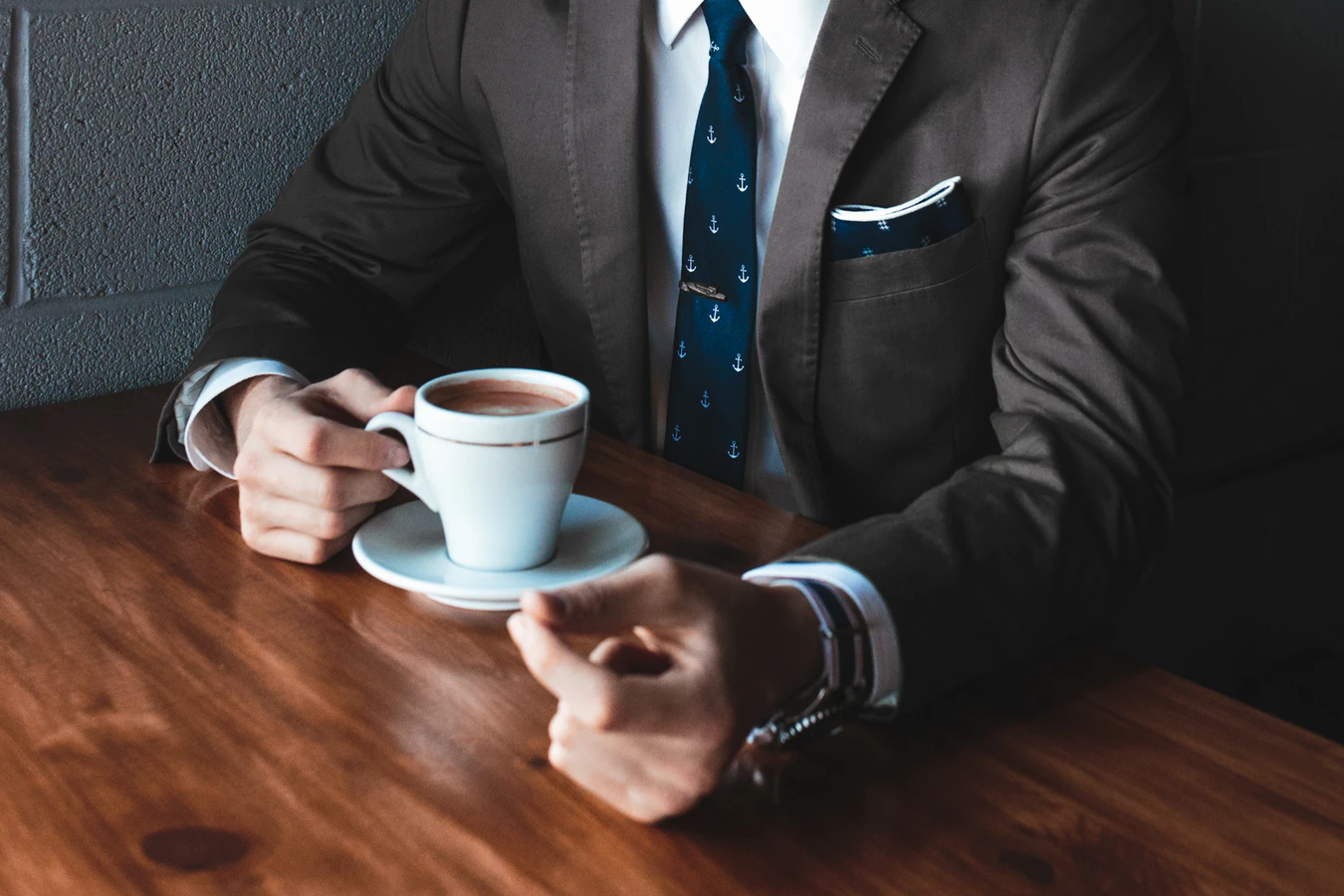 Person in a formal suit drinking coffee at a brown table