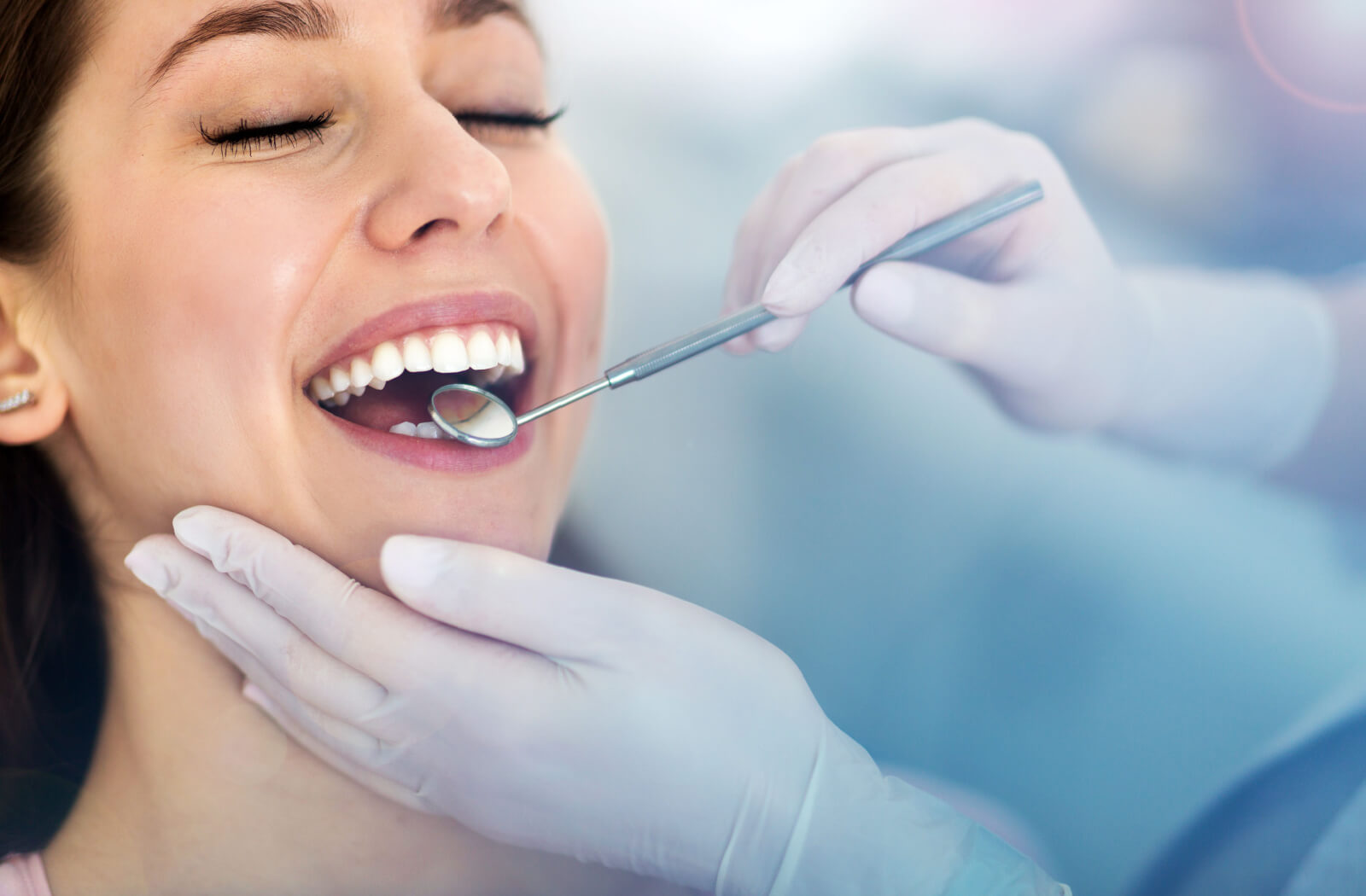 A close up of dentist hands with dental mirror checking up a woman's teeth at a dental clinic.