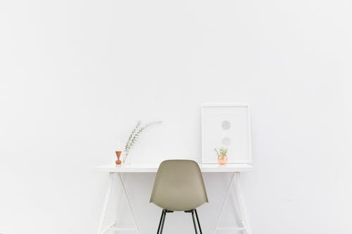 Minimalist white desk with small pot plant and frame on it