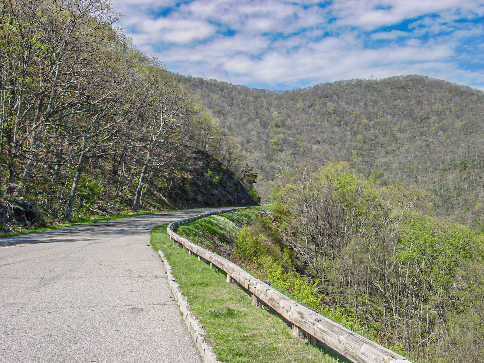 A road curves up a mountain slope with a wooden guardrail. 