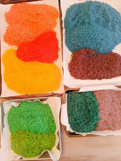 Dyed rice air-drying on a paper towel inside of several different pans. 
