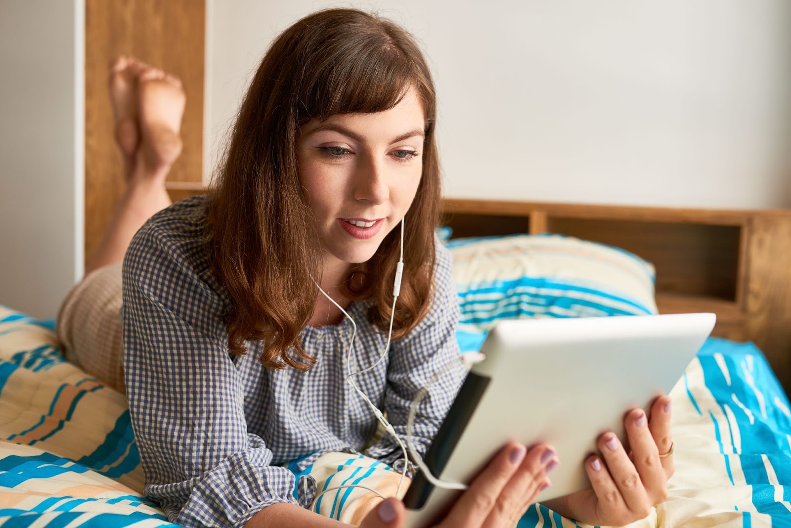 Smiling young woman lying on bed and watching show or sitcom on digital tablet