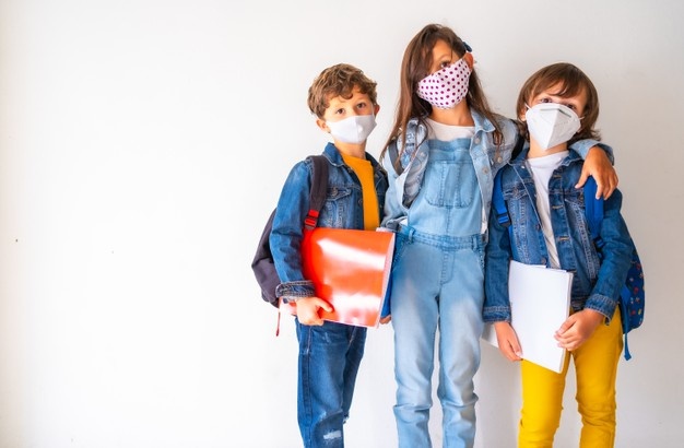 Kids with facemasks holding their school belongings and standing against a wall - covid-19 Free Photo