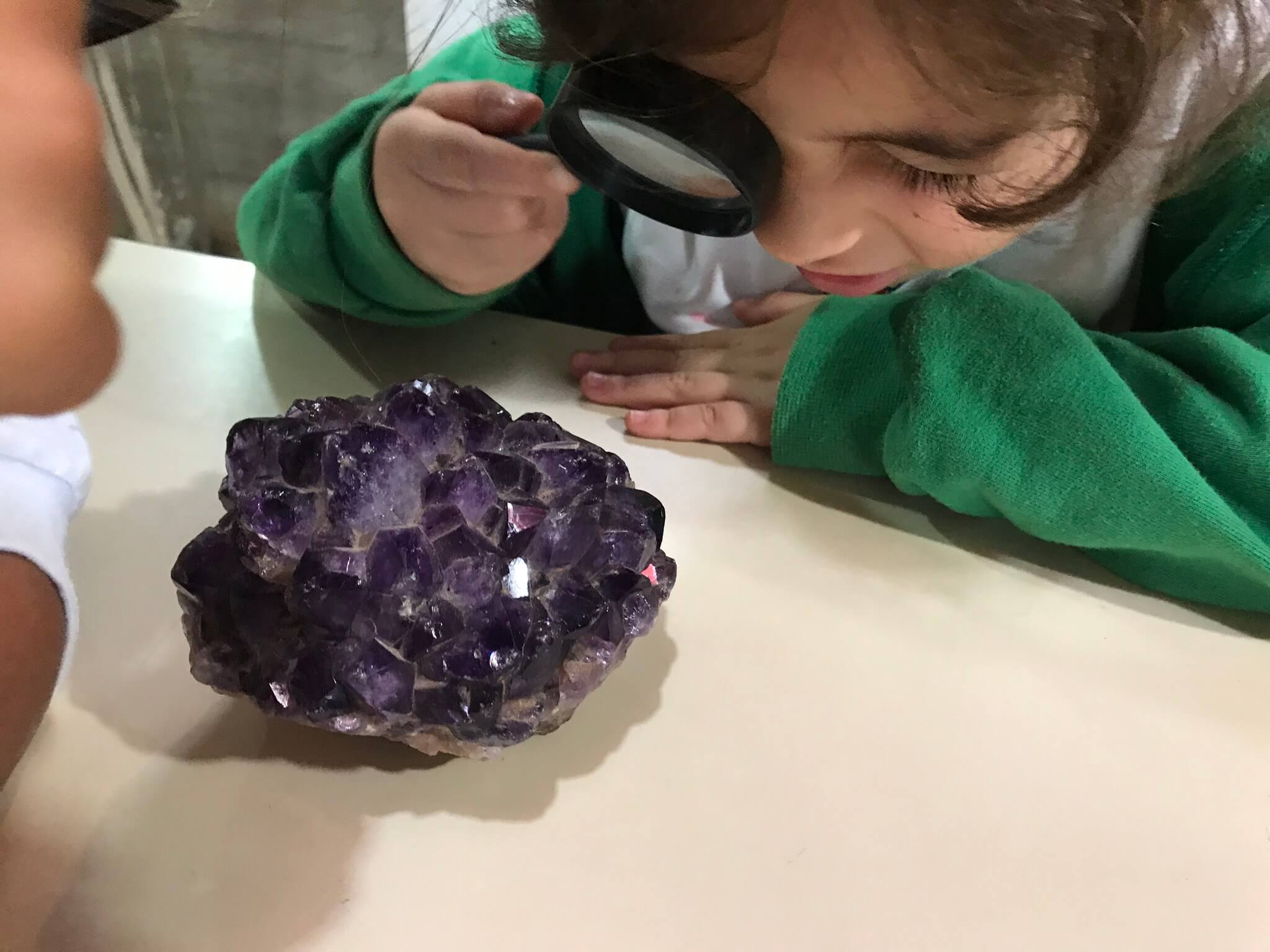 A imagem mostra uma criança observando uma pedra com lupa.
