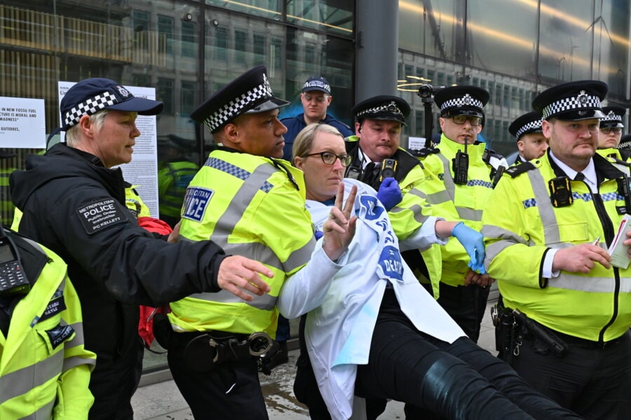 A scientist rebel makes the peace sign as a gang of police drag her away