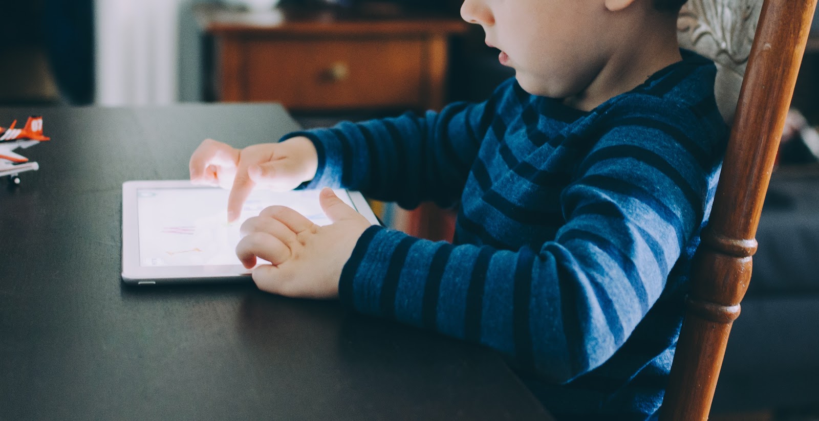 This is an image of a boy who is seated at a table using a tablet. This is what your child could look like after building a wifi robot at home with a robotics kit for kids.