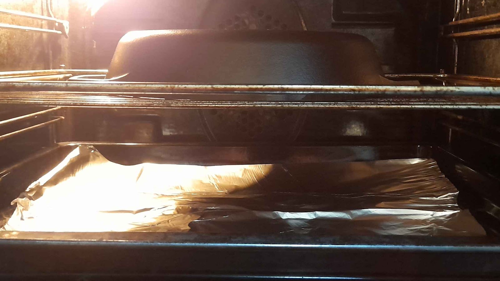 A skillet being seasoned in the oven upside down above foil.