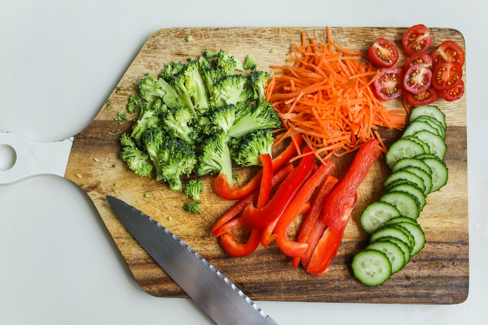 chopping board full of healthy food such as broccoli, carrots strips, cucumber, peppers and tomatoes