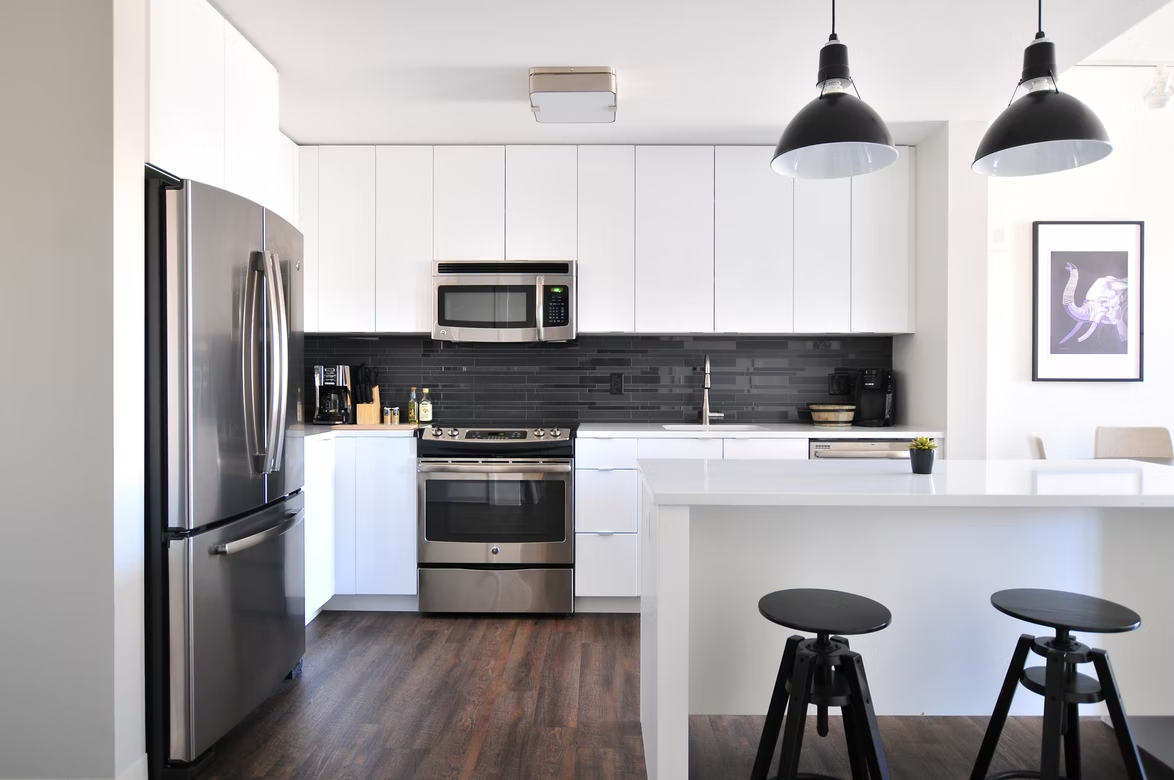 A kitchen with white drawers, silver fridge, white table, and black chairs