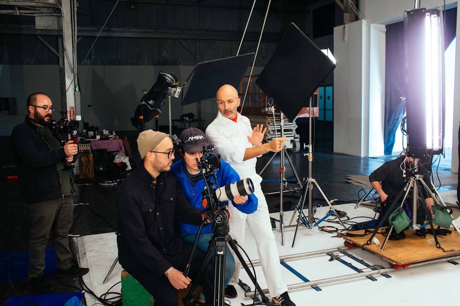 Photographer, Saam Gabbay, directs a shoot on a sound stage. You can see him surrounded by equipment including lights, dollies, and cameras.