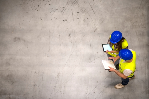 top-view-two-industrial-workers-wearing-hardhats-reflective-jackets-holding-tablet-checklist-gray-concrete-floor