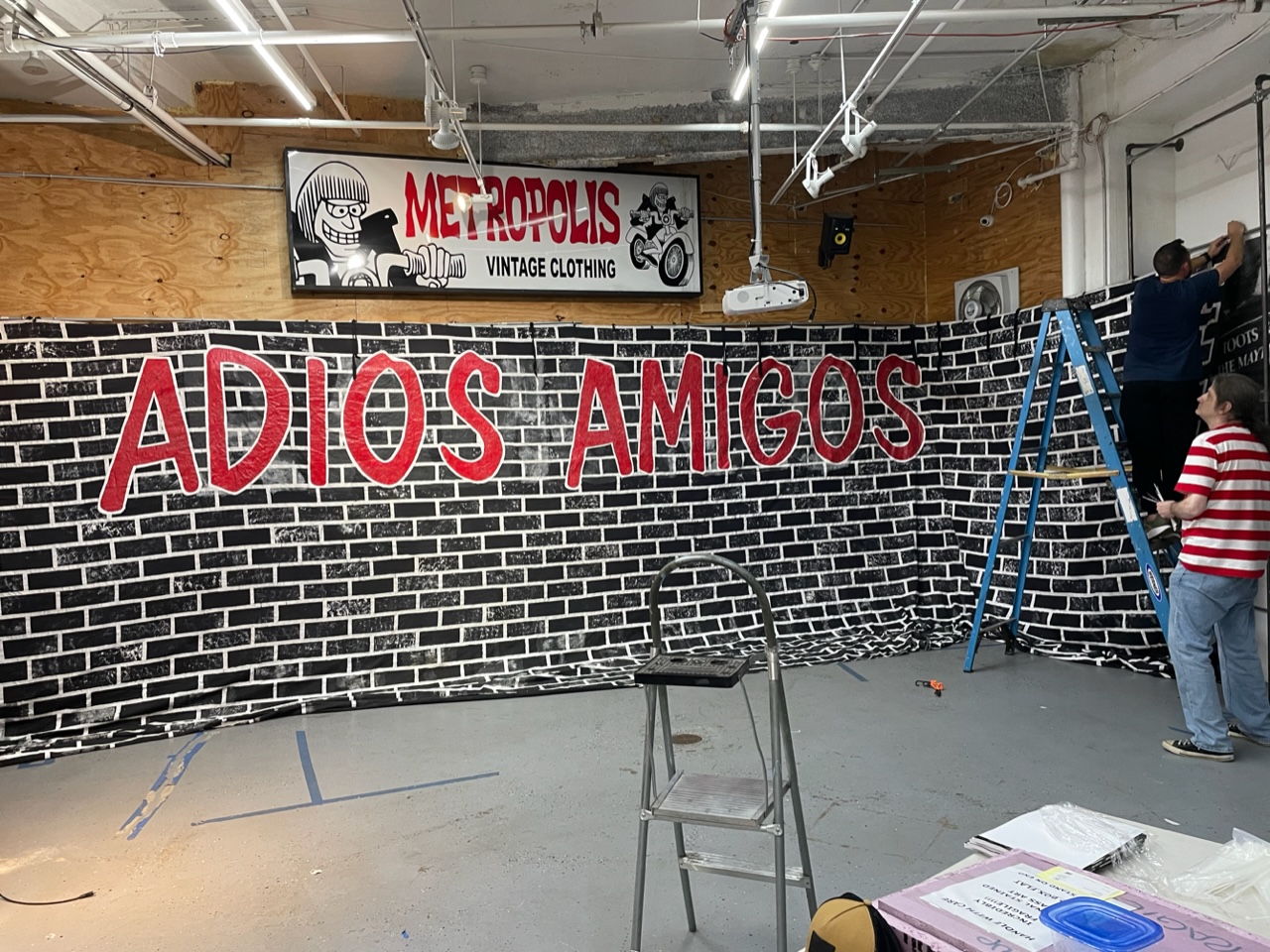 The Ramones’ final tour banner painted with a black and white brick background and bold red lettering of the words, “Adios Amigos,” being hung up at Metropolis Vintage in New York City. The massive banner measures approximately 36’ by 10.5’. RR Auction sold this lot for $12,805