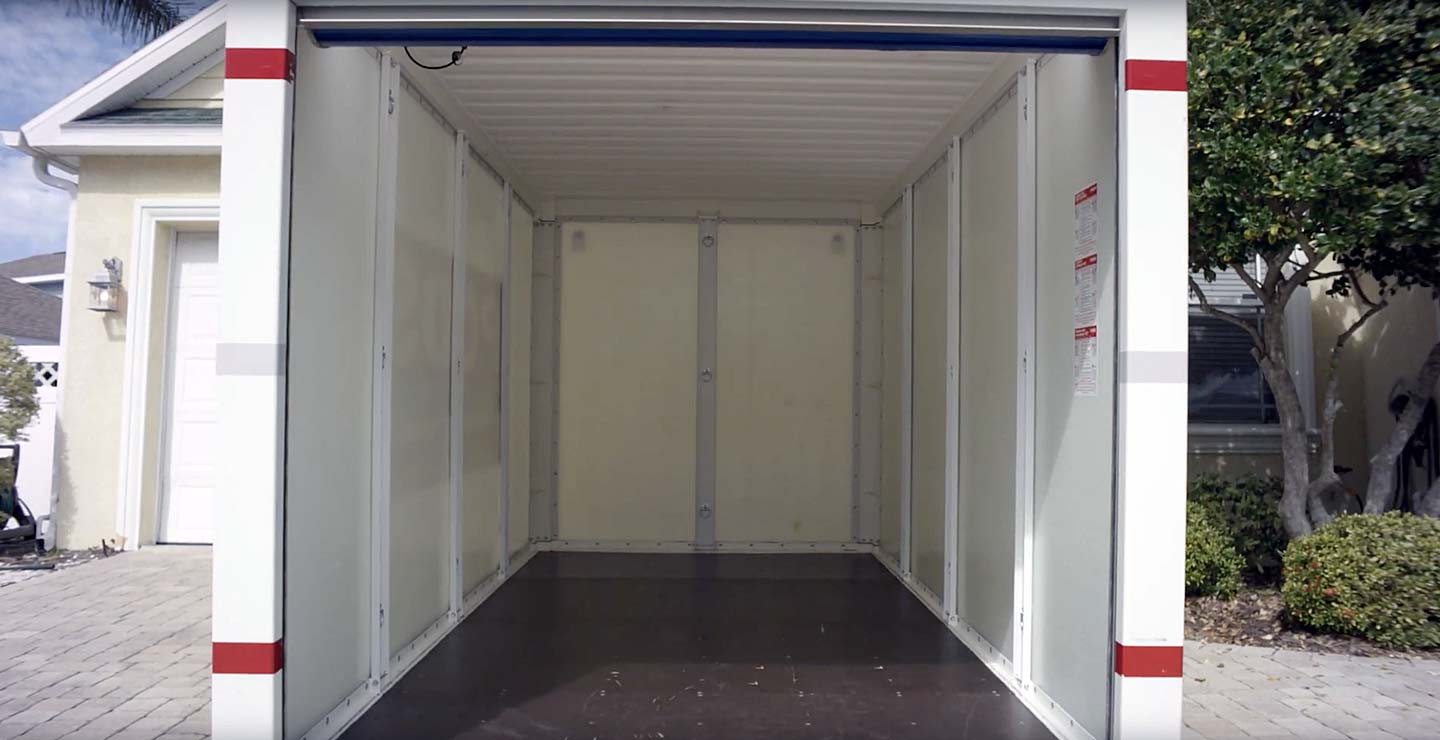 A PODS portable storage container sits empty in a residential driveway, waiting to be loaded with items.