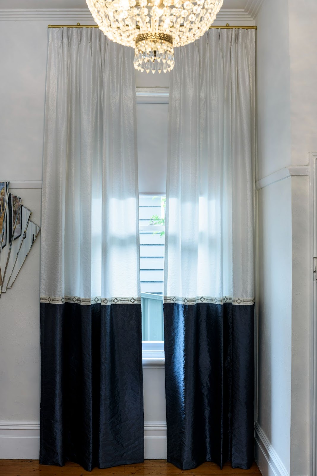 Two-tone curtains with white tops and dark bottoms, hanging in front of a window, with a chandelier above
