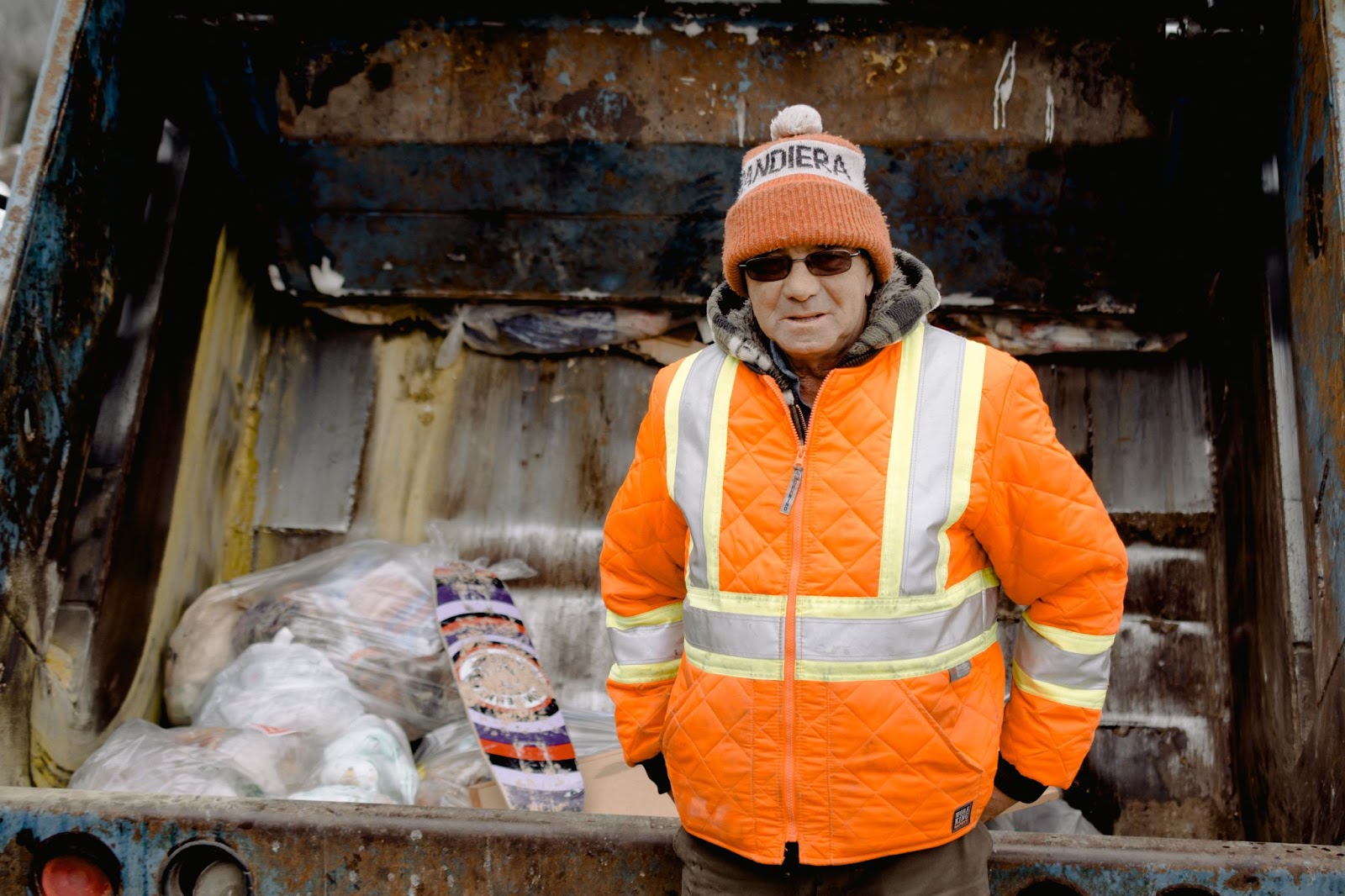 A man wearing fluorescent safety gear in front of a trash truck