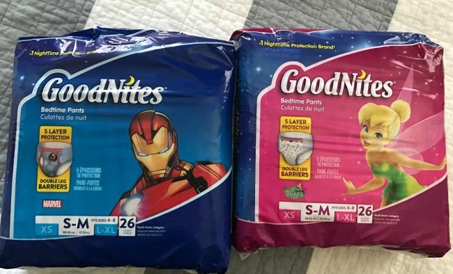 Two packages of GoodNites pull up sitting on a bed.