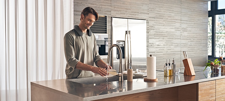 Man washing dishes in a kitchen while listening to SRS-NS7 wearable speaker