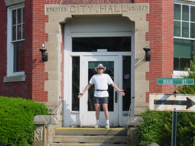 Man stands on the steps of a City Hall with arms out. 