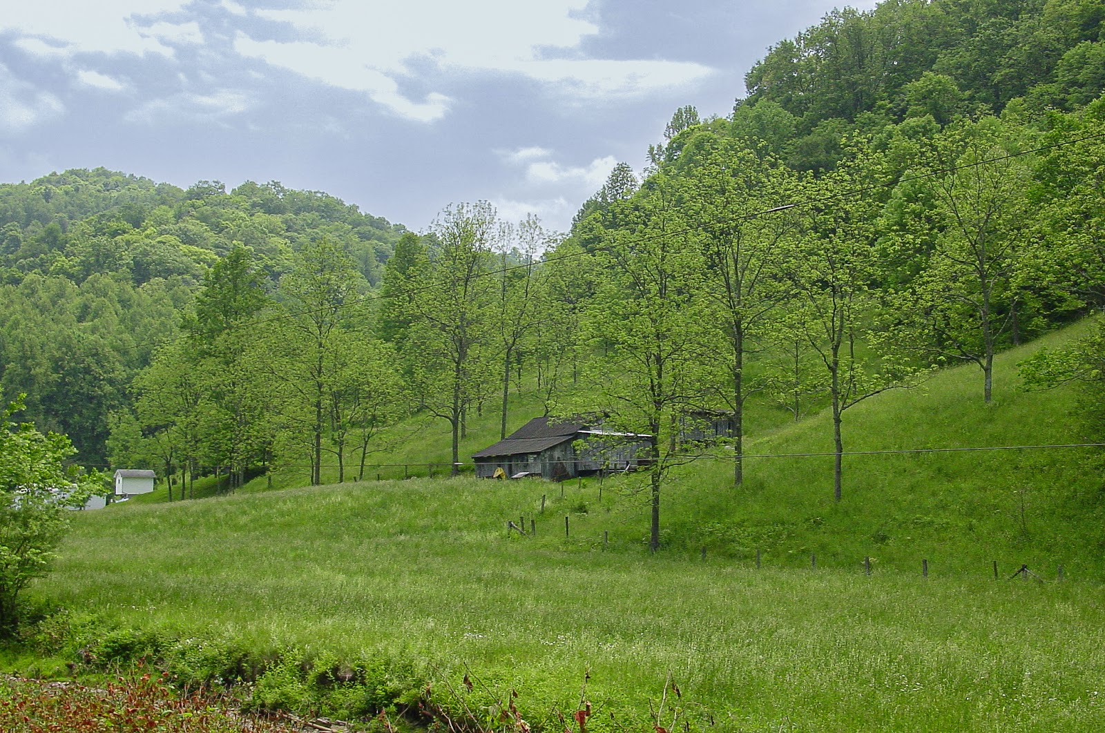 A weathered wooden home on a slope of surrounding green hills. 