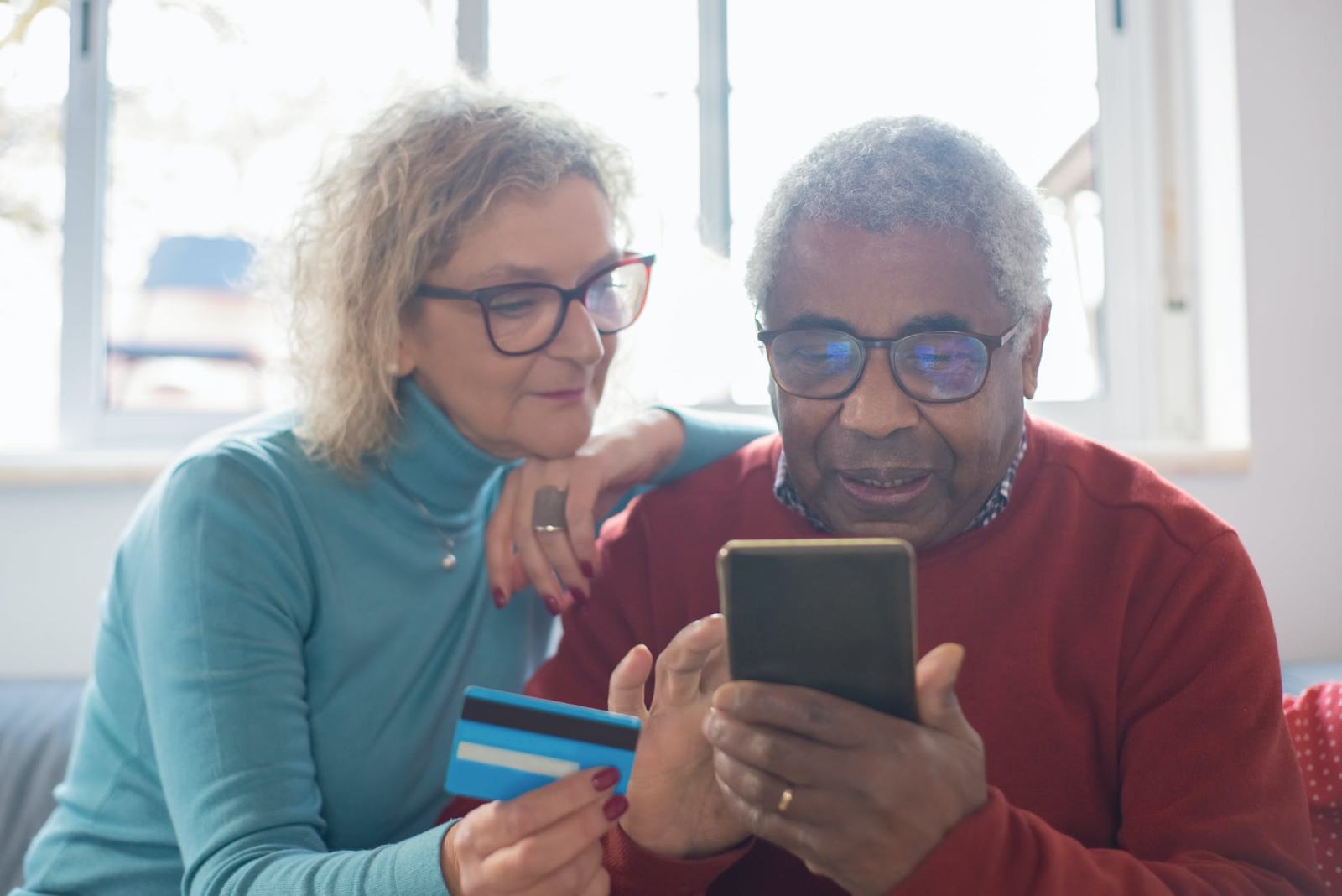 Bi-racial older couple looking at a mobile phone holding a credit card, as if making payments or checking their loan details. 