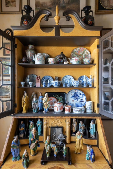 A vignetted of a styled cupboard filled with Chinese porcelains and mudmen.