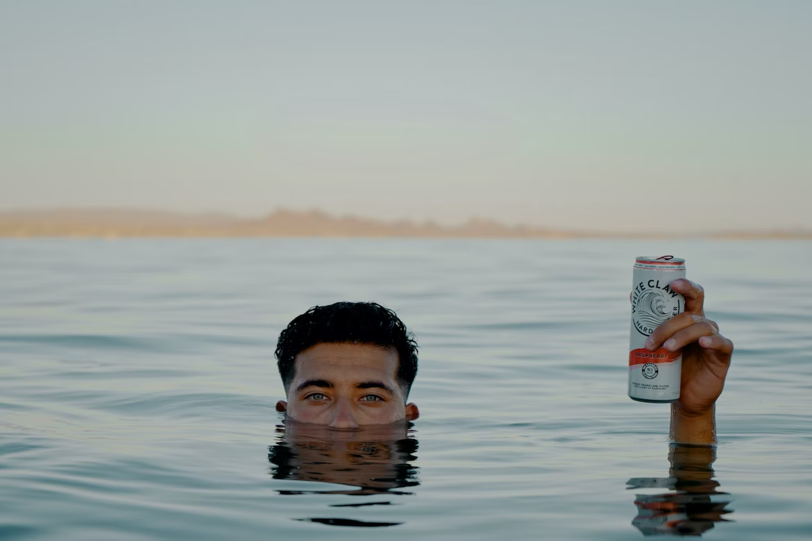man holding drink in water, lake, pond, swimming, sunburn, summer, beach, healing, sunscreen