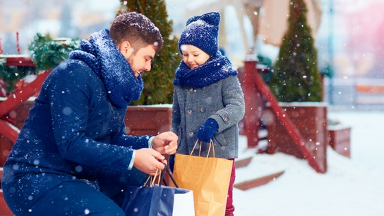 A man sitting on a bench in a snowstorm with a shopping bag with a young girl looking on.