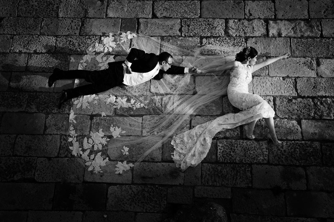 Black and white capture of a bride and groom posing as superheroes while lying on the ground 