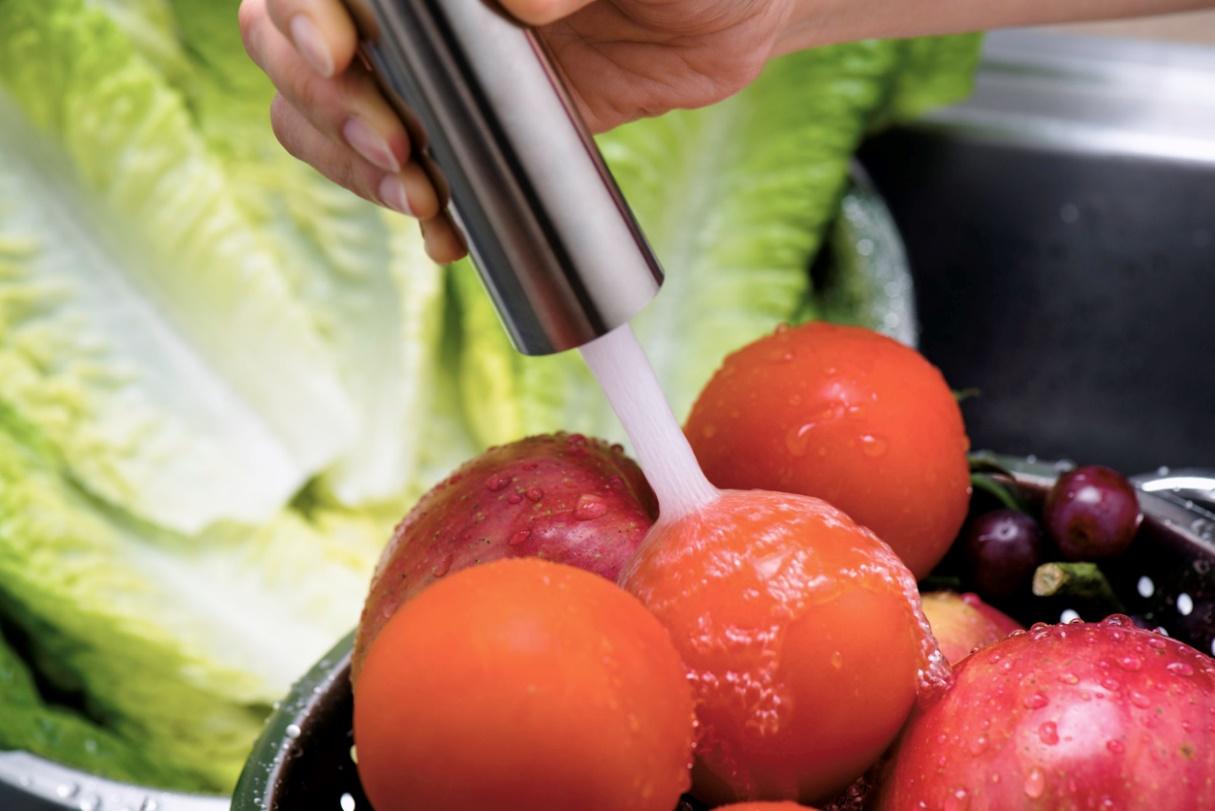Person washing vegetables with a faucet with a pull-down sprayer