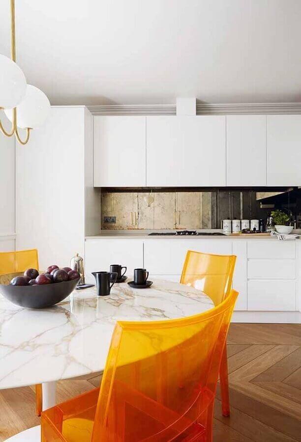 Cozinha com armários brancos, piso de madeira, mesa redonda de mármore e cadeiras amarelas.