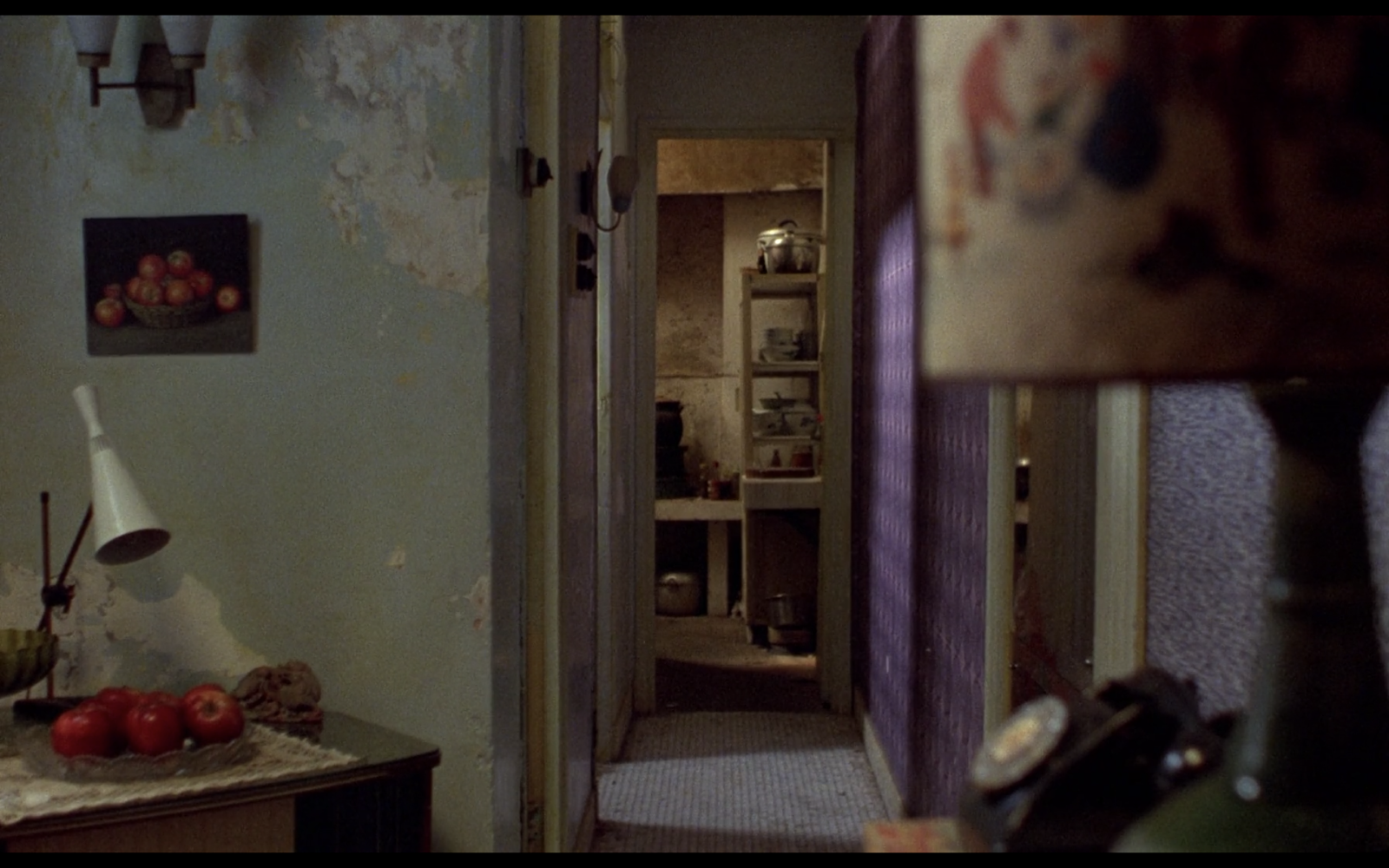A screen still from the film In the Mood for Love, featuring a look down a narrow hallway of an apartment. No characters are in sight.