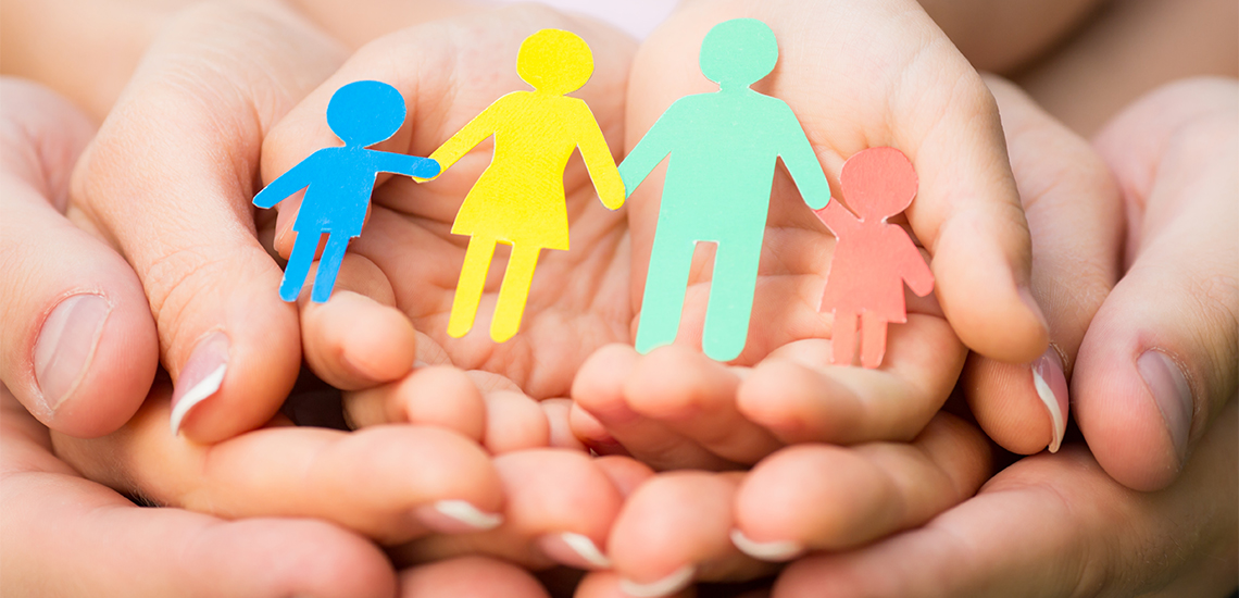 Hands holding a paper cutout of a family.