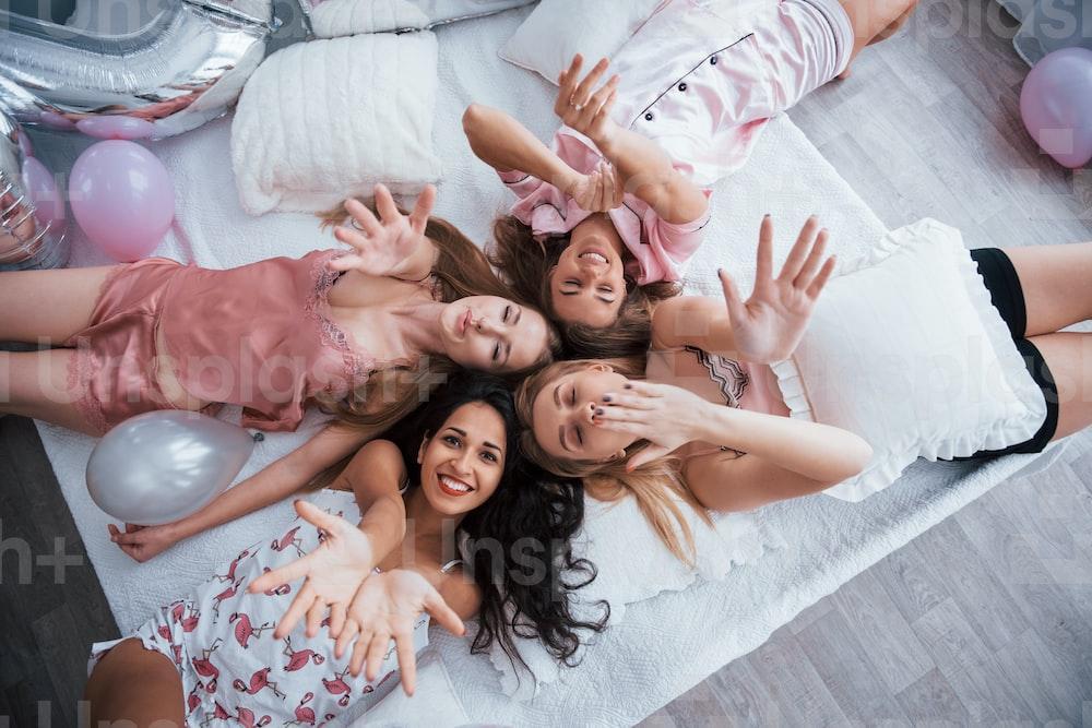 These beautiful friends wish you happy holidays. Top view of young girls at bachelorette party lying on the sofa and raising their hands up.