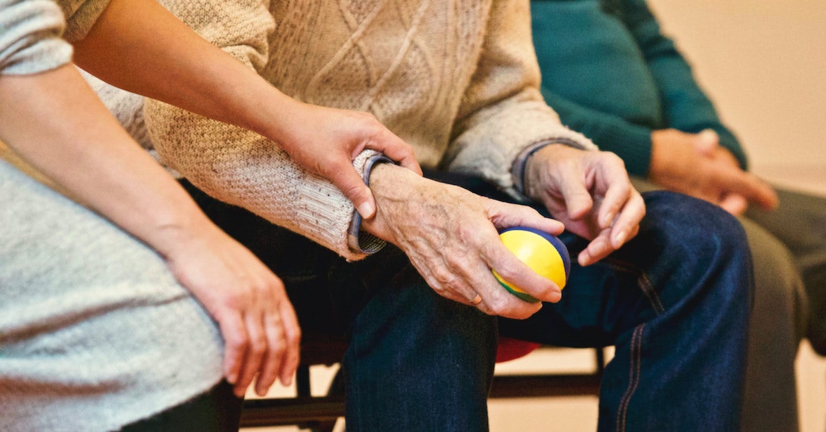 Someone holds the arm of an elderly person squeezing a ball.