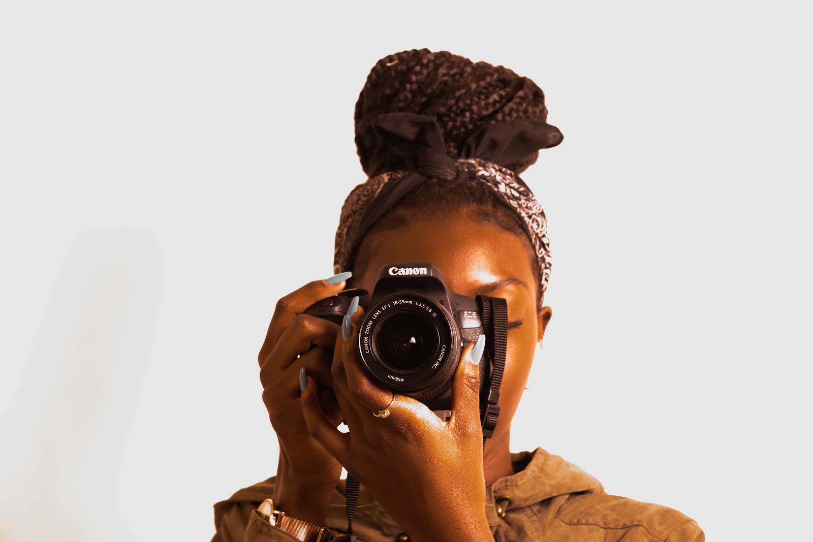 a woman in a beige jumper holding a Canon DSLR up to her eye