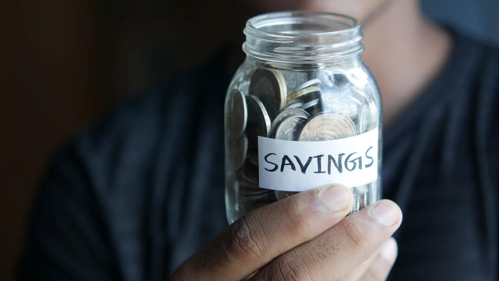 A man holding a jar of coins with the word "savings" written on it.