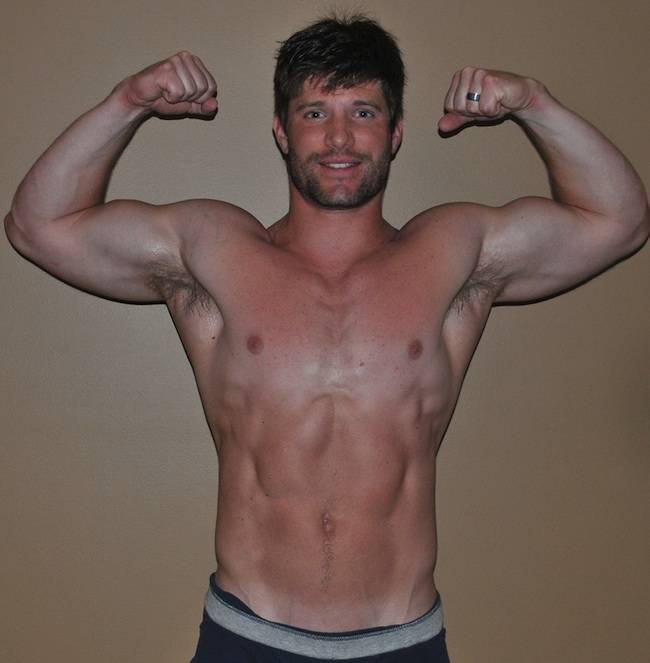 male fitness model flexes his arms for the camera while posing shirtless in a pair of grey boxers
