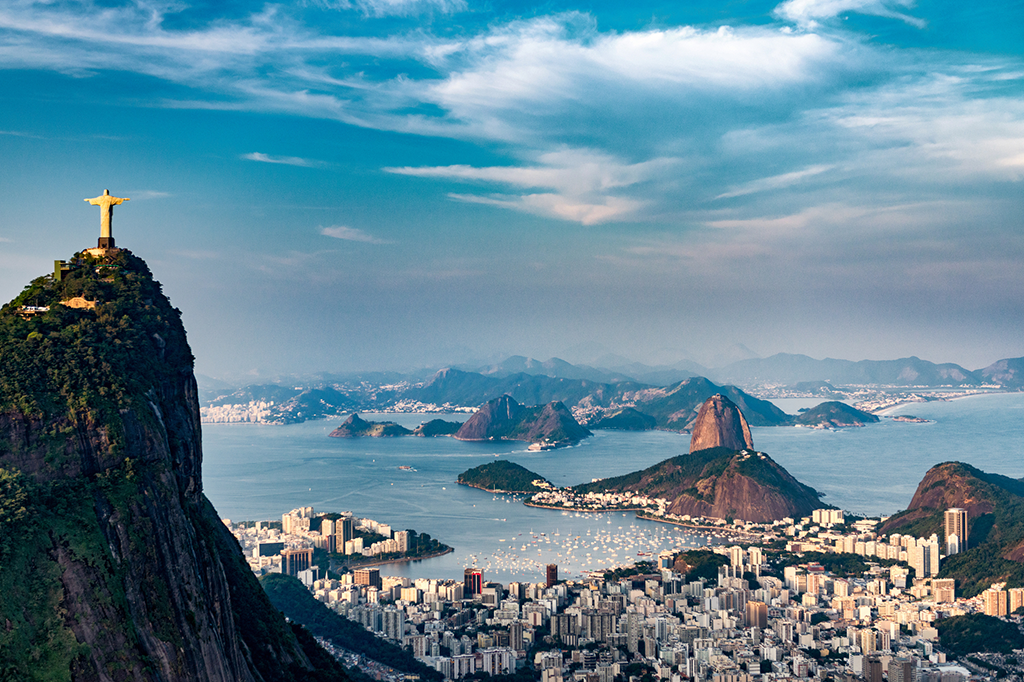 Imagem do cristo redentor e o pão de açúcar ao fundo, com mar e prédios ao fundo. 