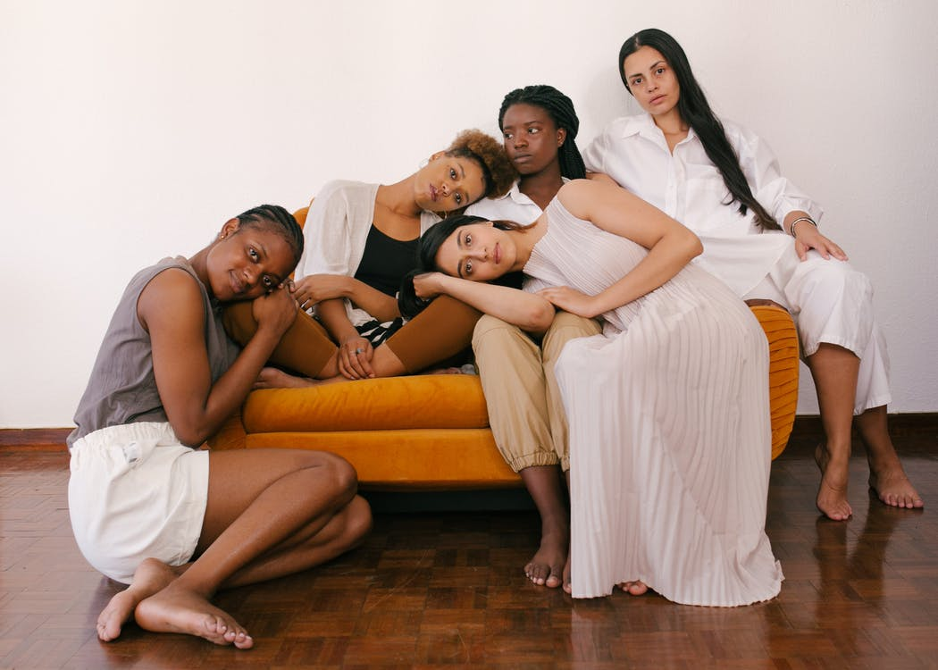 Image of five women leaning against each other on an orange couch.