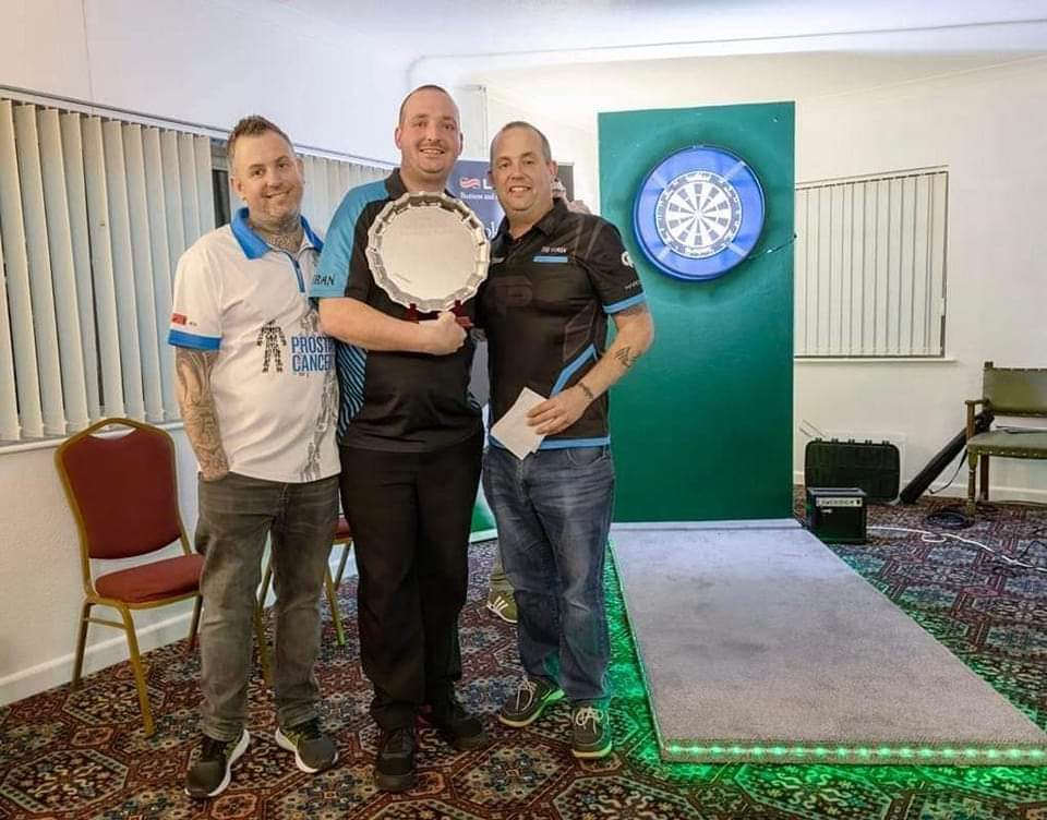 A group of men standing in front of a dart board
Description automatically generated with medium confidence