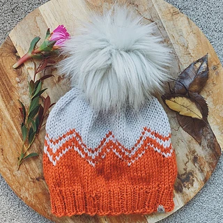 orange and white hat with large fur pom pom on wooden background