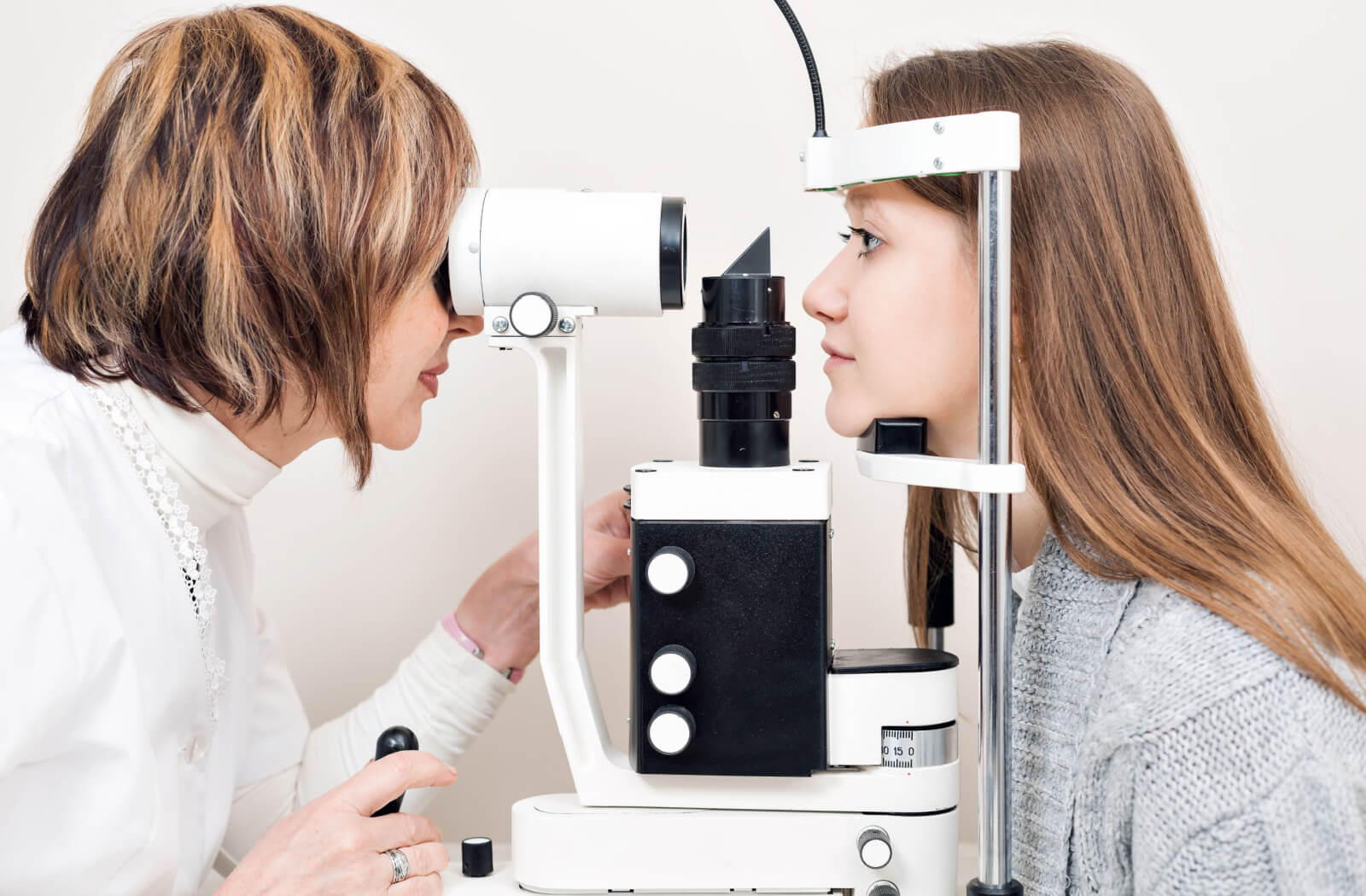 A female optometrist examining the eyes of a young woman using a medical device to detect potential eye problems.