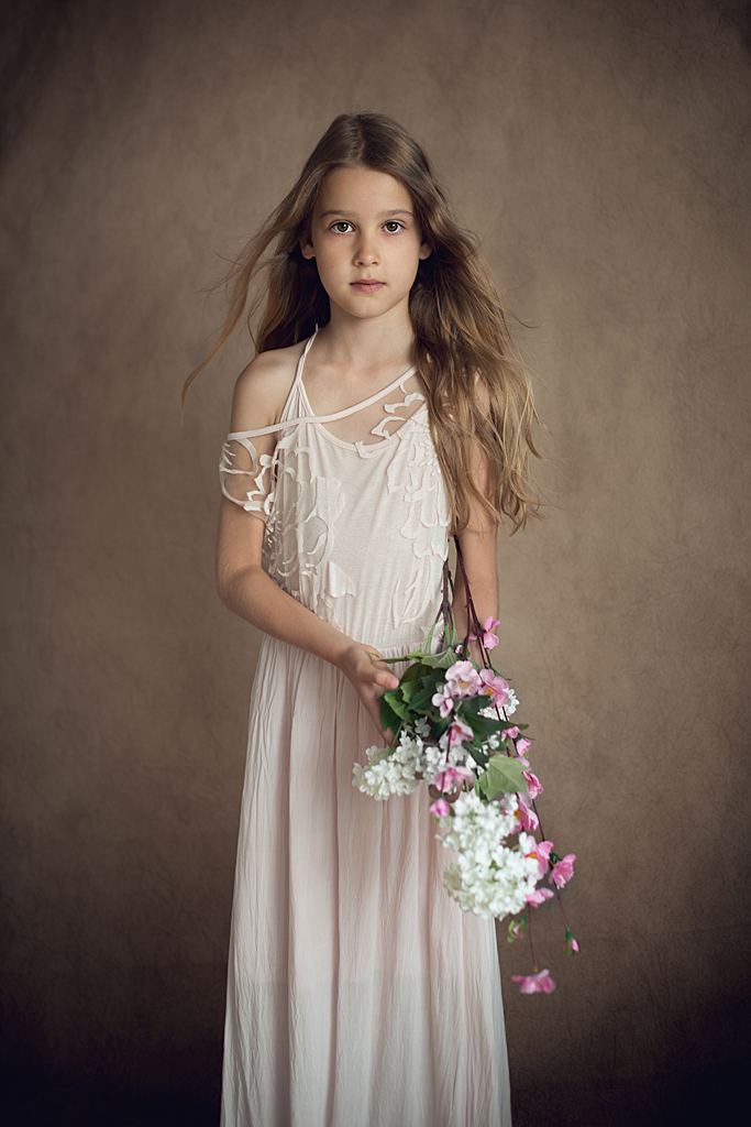 Meisje met lange haren en in een lange jurk houdt bloemen vast.