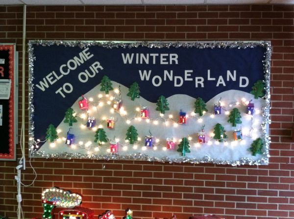 a welcome to our winter wonderland bulletin board with lights, trees, and houses scattered on a snowy hill 