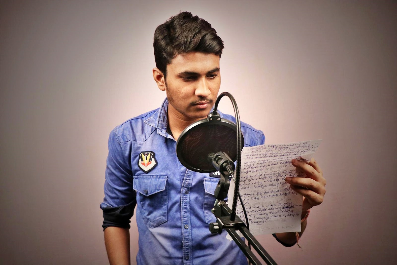 An image of a voice over actor reading a script in in front of a microphone in a studio.